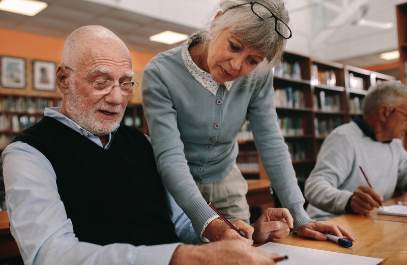 Senior student getting a college degree with a senior teacher in the library